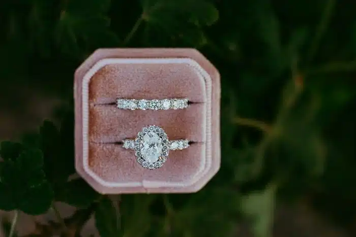 oval halo engagement ring and diamond band displayed in a pink velvet ring box surrounded by green foliage