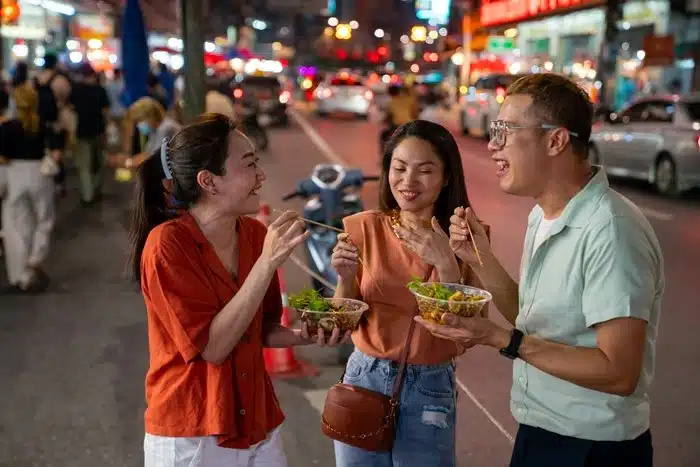 a group of tourists enjoying street food together during a guided tour in Bangkok at night