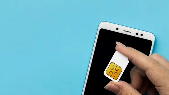Hand holding a SIM card next to a smartphone — the easiest way to set up mobile data for Euro trip travel