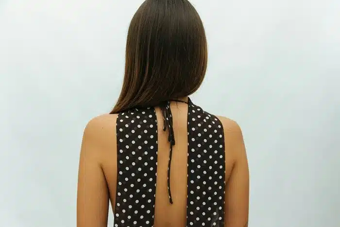 Back view of a woman wearing a black and white polka dot tied-back halter neck top with an open back