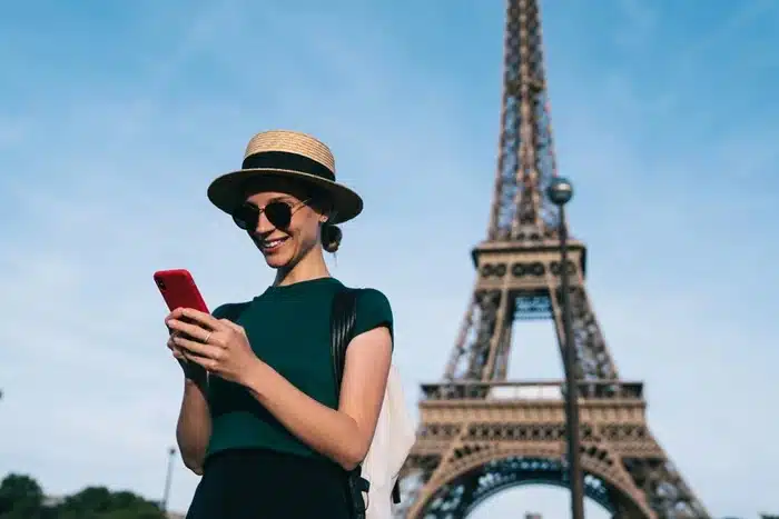 Woman in a straw hat browsing her phone with the Eiffel Tower in the background in Paris