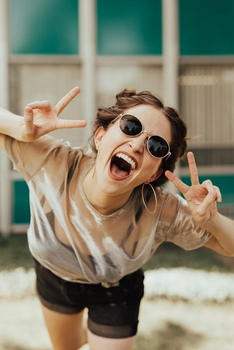 Happy young woman wearing sunglasses celebrating with peace signs and a joyful expression