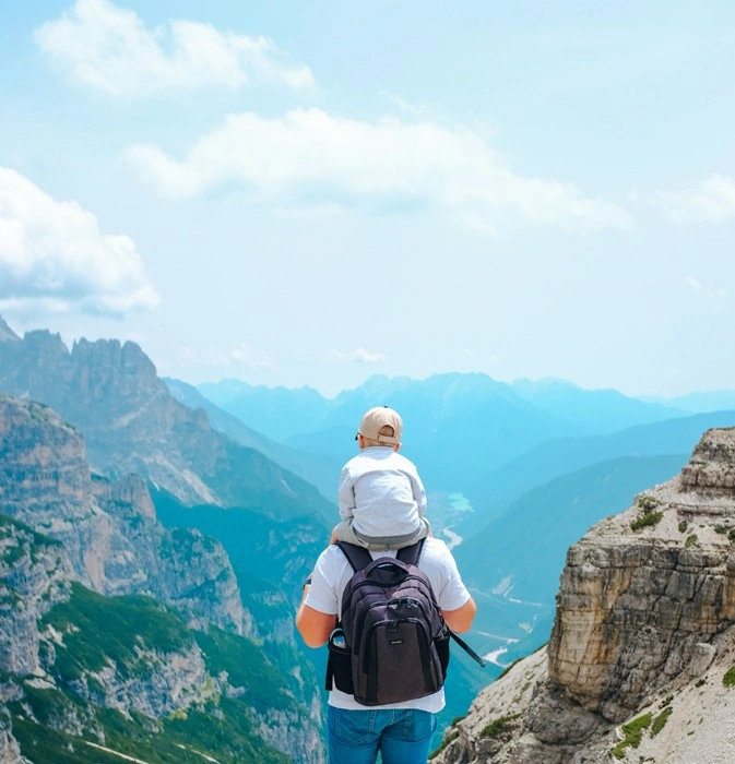 Father and toddler enjoying memorable travel destinations together, looking out over a stunning alpine valley from a mountain ridge