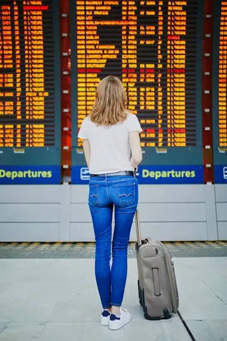 woman with luggage checking the departures board at an international airport