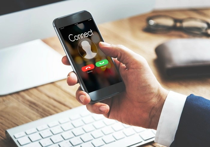 Person in a suit accepting an incoming call on a smartphone at a desk
