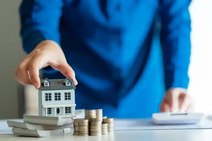 person holding a model house next to stacked coins and a calculator for cross-border investment and estate planning