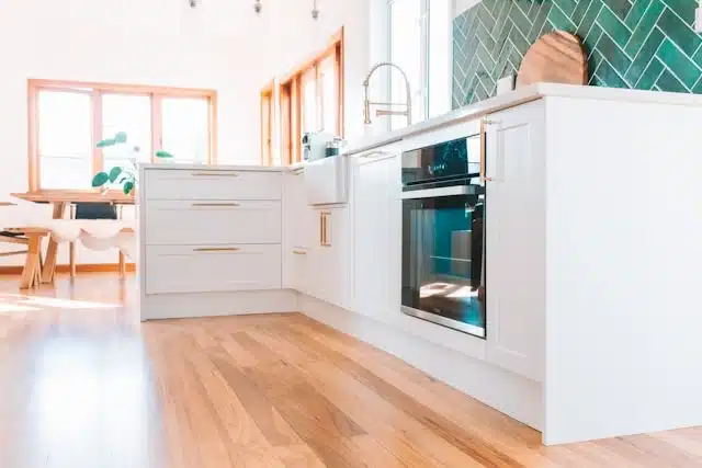 Bright modern New Zealand home kitchen with white cabinetry, green tile backsplash, built-in oven, and hardwood floors
