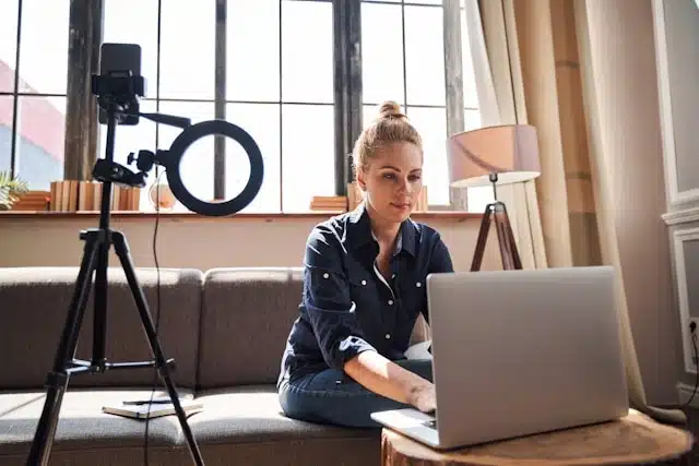 woman sitting on a couch with a laptop and a ring light on a tripod set up for a streaming session