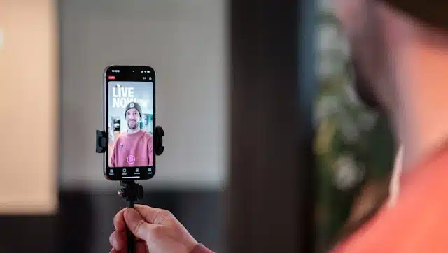 man holding a smartphone on a tripod showing a live now screen during a mobile stream
