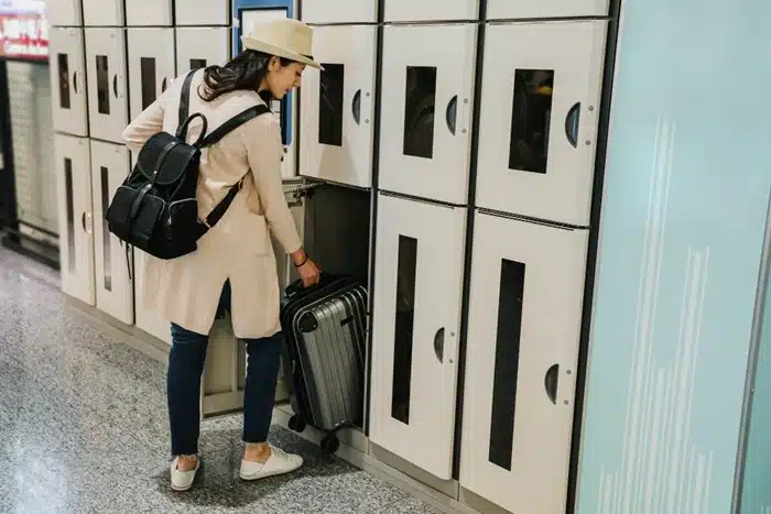 Woman storing a suitcase in a self-service luggage locker at a transit facility