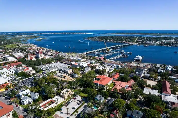 Aerial view of a Florida coastal town with a marina slip, bridge, and sailboats on a wide blue bay on a clear day