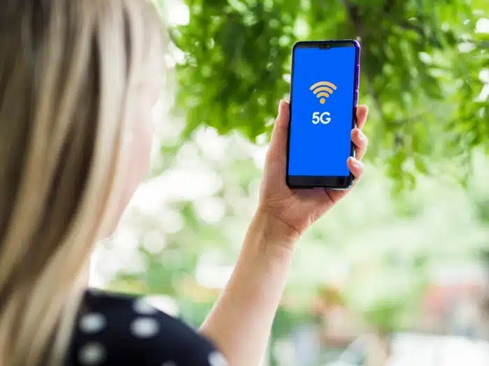 Woman holding a phone displaying a 5G signal icon outdoors, representing fast mobile data speeds while traveling