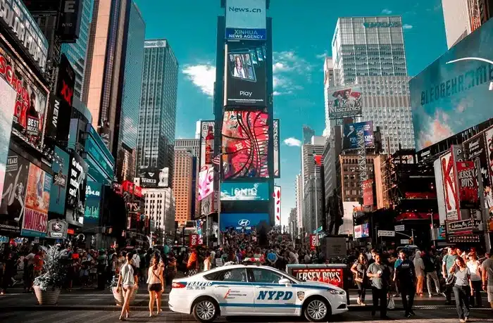 Busy Times Square in New York City with crowds of visitors, bright billboards, and an NYPD police car on the street