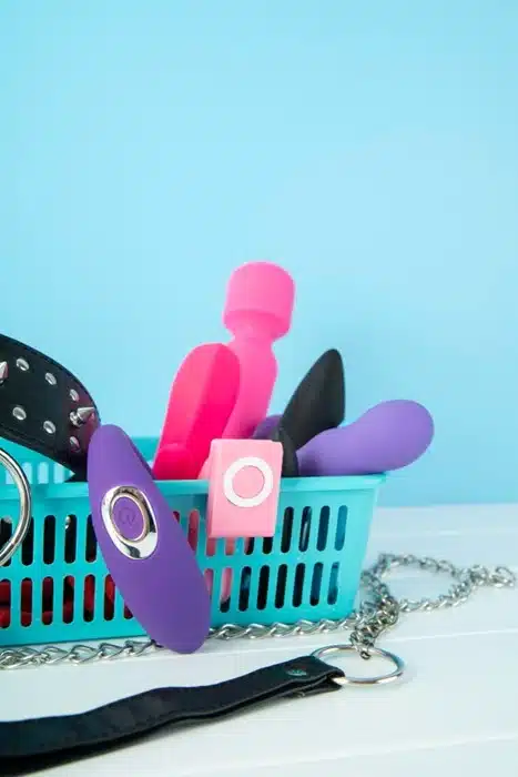 Assorted silicone sex toys in a teal basket with restraint accessories on a light blue background