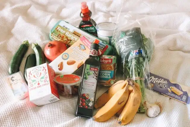 Online grocery order laid out on a white surface with fresh vegetables, fruit, pantry staples, and packaged goods
