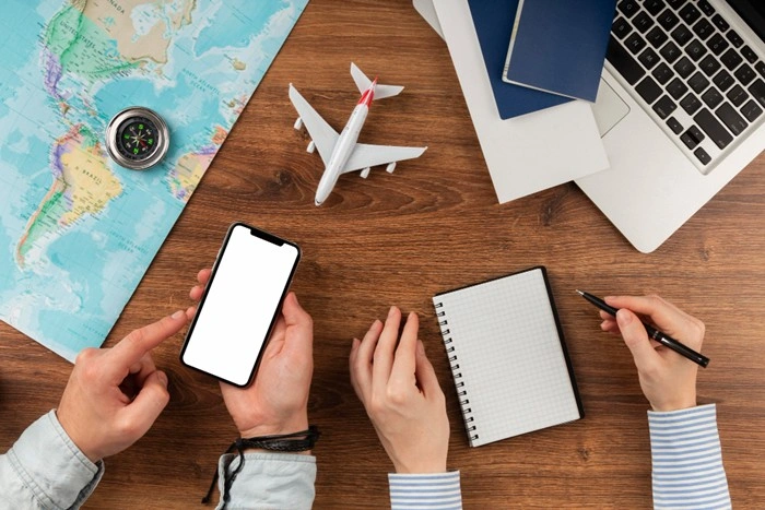 Outsourcing travel for business — two people planning a trip with a phone, notebook, world map, and model airplane on a desk