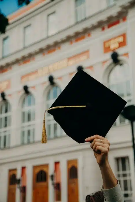 A hand holding up a graduation cap in front of a classic university building abroad