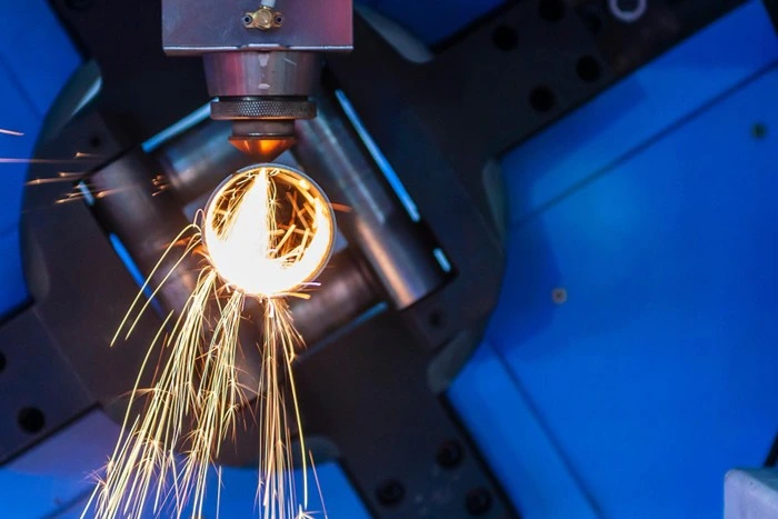 industrial plasma cutting machine head with glowing arc and sparks against a blue workshop background