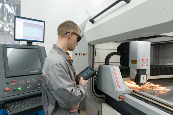 technician operating a CNC plasma cutter with safety glasses in a modern metal fabrication facility