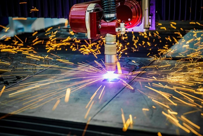 robotic plasma cutting arm producing a bright arc and wide spray of sparks across a large steel plate in an industrial setting