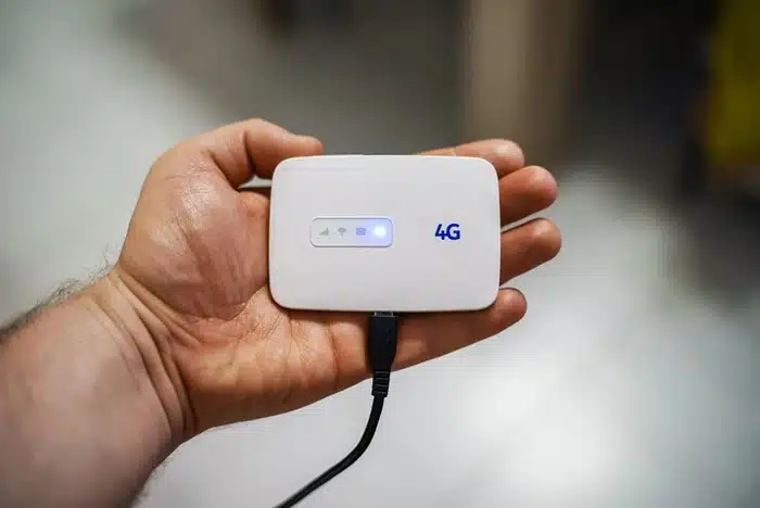 Hand holding a compact 4G pocket WiFi device with a charging cable, ideal for staying connected while traveling