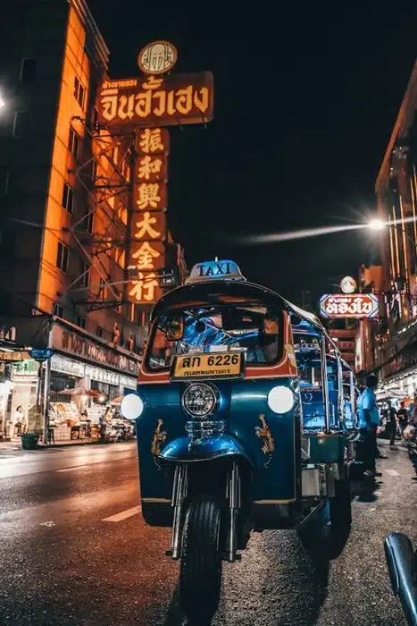 a blue tuk-tuk taxi on a busy Bangkok street at night surrounded by neon signs