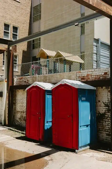two portable toilets against a brick wall representing basic sanitation in rough living conditions