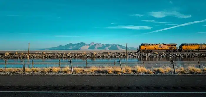 yellow freight train passing through Utah desert landscape with mountains and lake in the background
