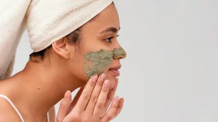 woman applying a clay exfoliating mask at home as part of her skincare routine