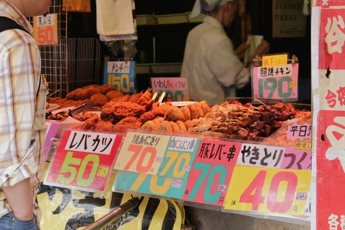 Colorful Japanese street food stall displaying fried snacks and skewers with bright price signs in yen