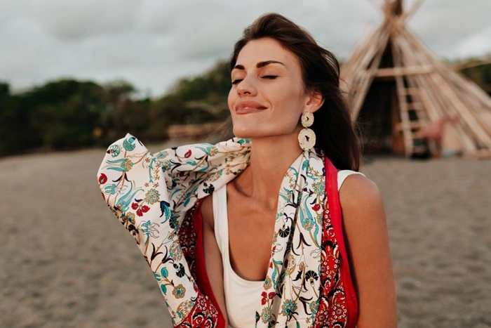 Woman wearing stud earrings for travel at a boho beach setting, styled with a floral kimono and white top