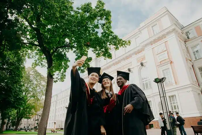 Three diverse international graduates in caps and gowns taking a selfie outside a university building — study abroad trends 2026