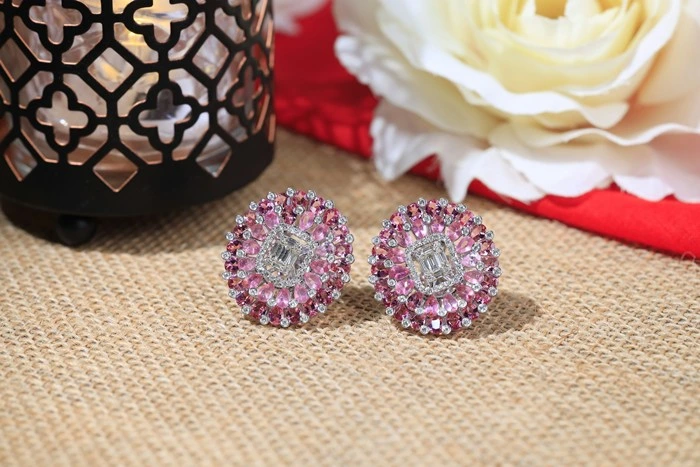 Stylish pink gemstone stud earrings with silver setting displayed on a textured surface with floral décor