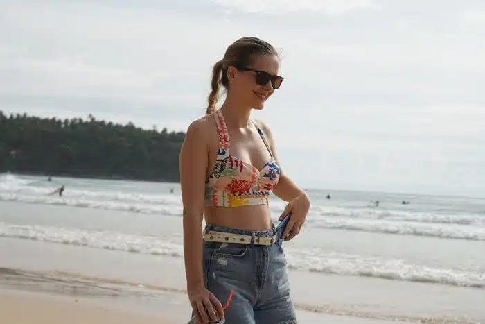 Stylish traveler wearing a printed halter top for warm-weather destinations, paired with high-waist denim shorts on a tropical beach