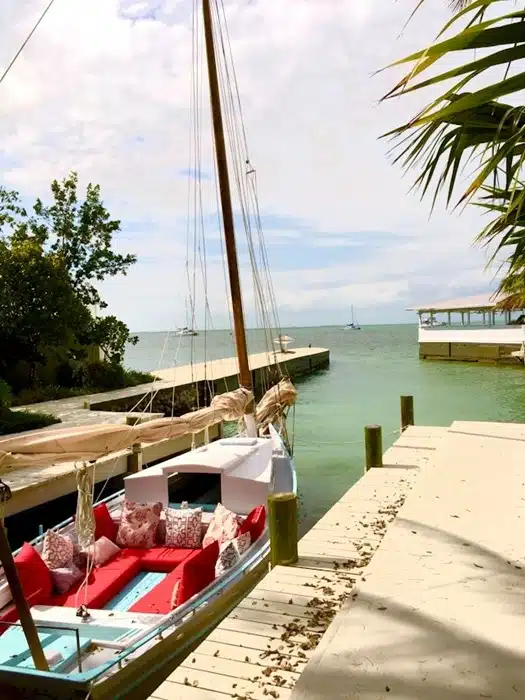 A styled boat docked at a private slip beside a vacation house in Florida with clear turquoise waters and sailboats in the distance