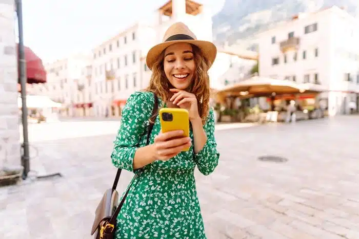 Happy woman traveler checking her yellow phone while standing in a picturesque European city center