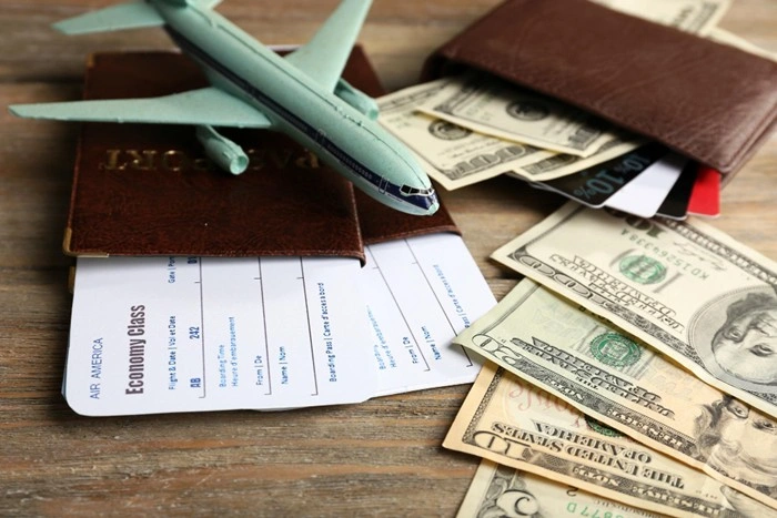 Travel documents including a passport, economy class flight ticket, and cash next to a model airplane on a wooden surface