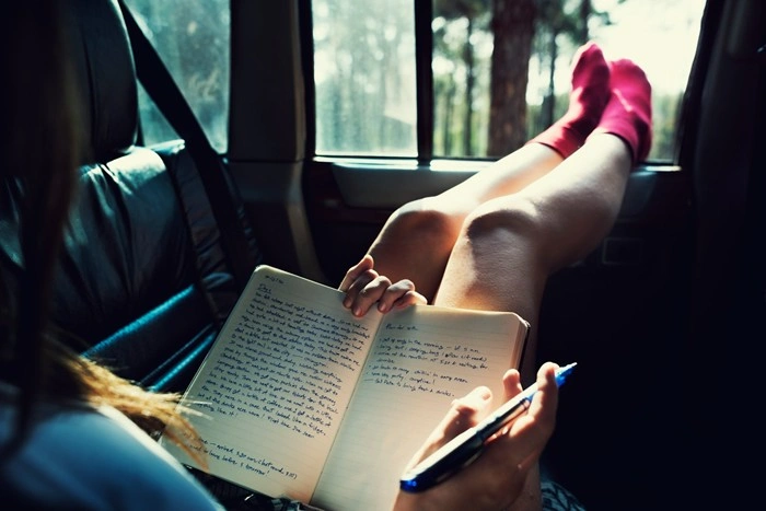 Female traveler writing in a journal while relaxing in the back seat of a car during a road trip