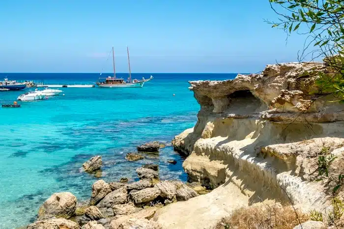 Traveling to Protaras, Cyprus — rocky coastline with crystal clear turquoise water and sailing boats