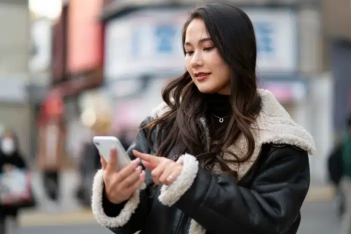 woman checking her smartphone while walking on a street in Asia