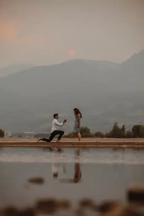 man kneeling to propose beside a reflective pool at dusk with misty mountains in the background