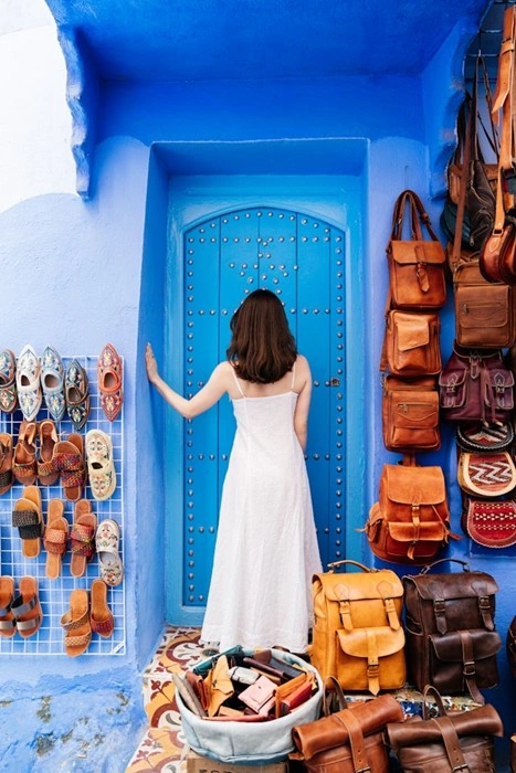Female traveler exploring a colorful blue-walled souk in Morocco with leather goods and handmade sandals on display