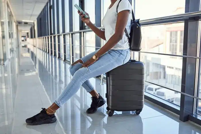 traveler seated on a suitcase scrolling on smartphone in an airport corridor