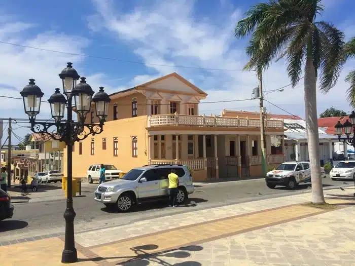 A silver SUV in a charming Dominican Republic town centre with ornate street lamps and a yellow colonial building