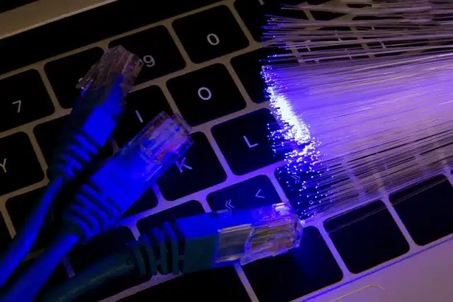 ethernet cable and glowing fiber optic strands side by side on a laptop keyboard showing the difference between cable and fiber internet