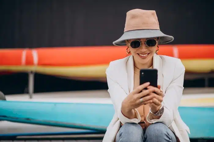 Trendy female traveler using her phone outside with vibrant kayaks in the background