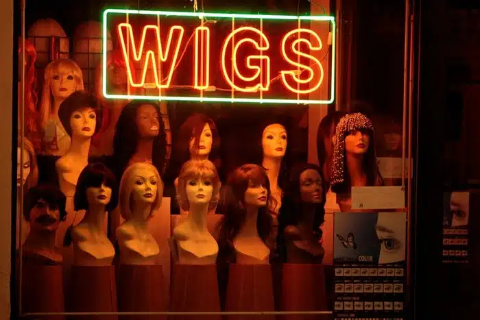 Wig shop window display with mannequin heads wearing various hair styles under a neon wigs sign