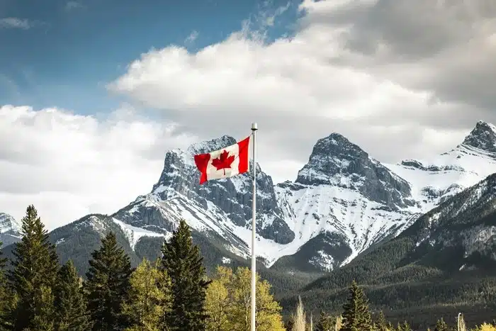 Canadian flag flying in front of snow-capped mountain peaks and evergreen trees