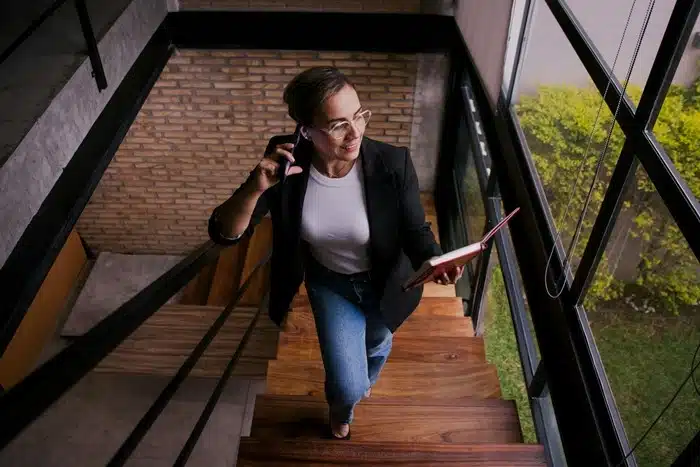 Woman in a blazer walking up the stairs while on a phone call and holding a notebook, illustrating how staying active in daily life adds up over time