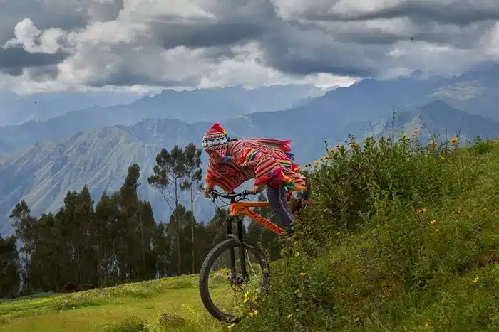 Young rider in colorful poncho biking through grassy hills with Andean peaks in the distance